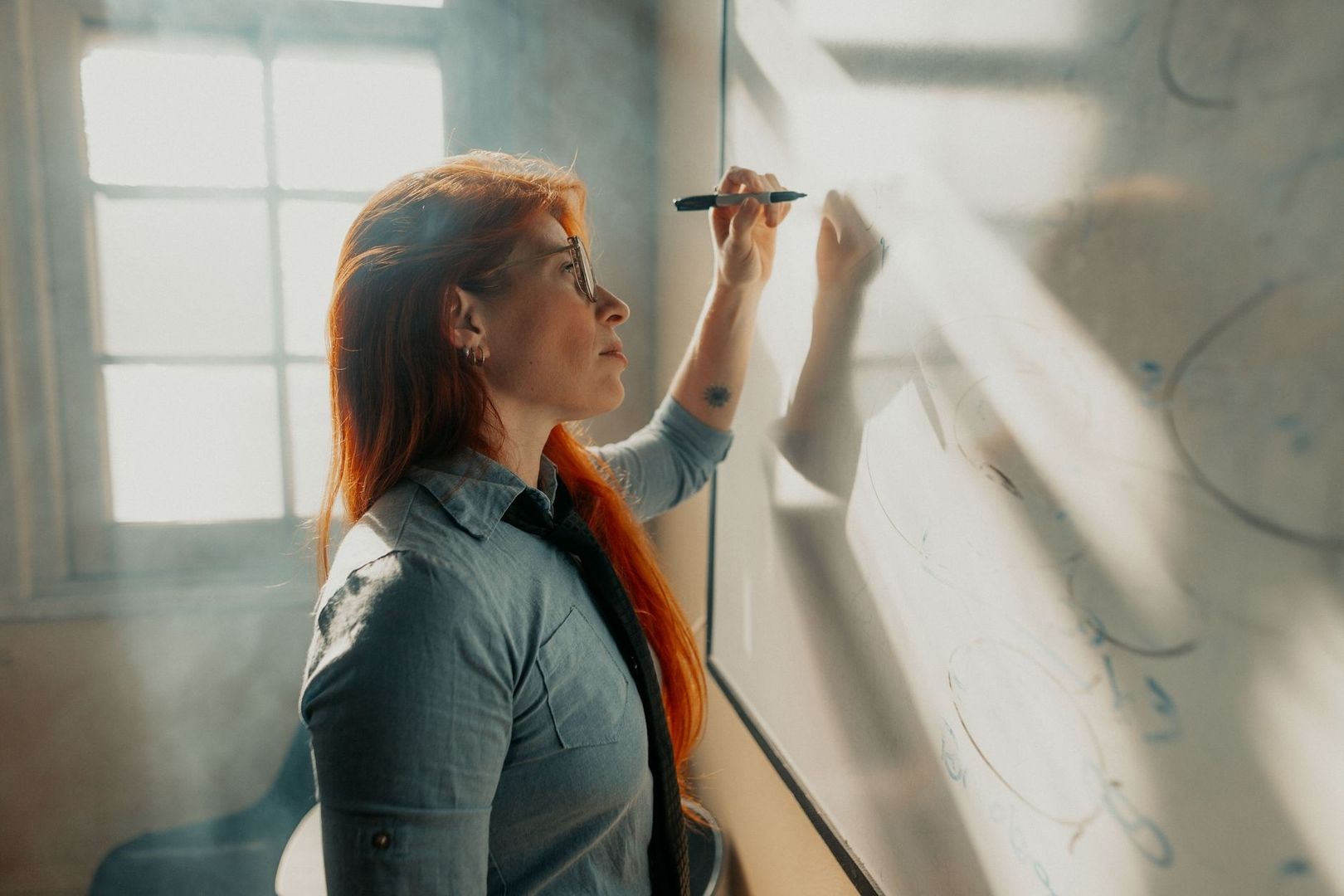 Woman writing on a transparent board in a sunlit office